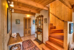 A wooden interior with a staircase, a wooden table, and a rug.