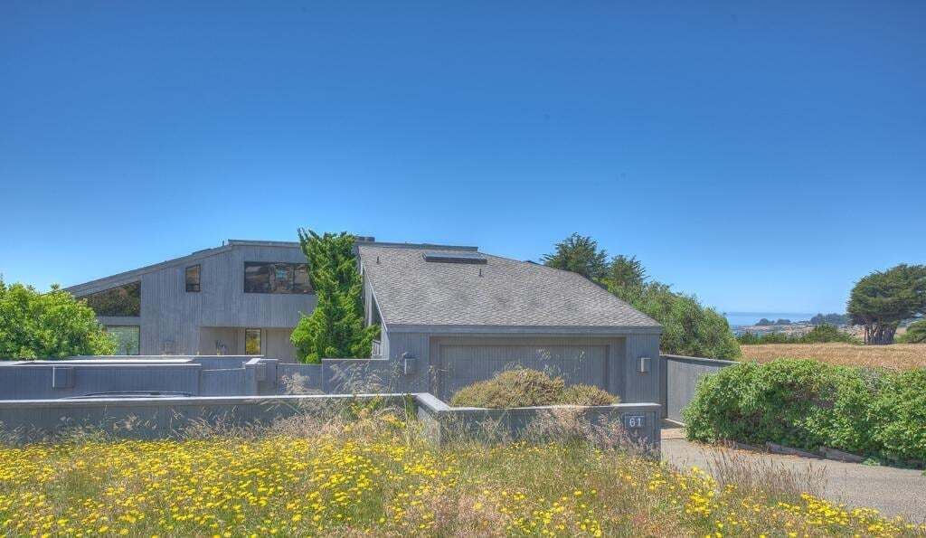 A modern two-story house with a garage, surrounded by a well-maintained garden and a clear blue sky.