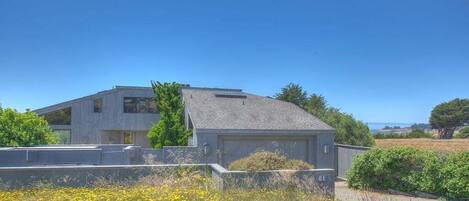 A modern two-story house with a garage, surrounded by a well-maintained garden and a clear blue sky.
