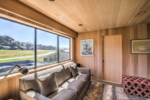 A modern interior with a wooden ceiling, large windows, a sofa, and artwork. - Wild Iris | Ocean View Haven with Hot Tub (Sea Ranch)