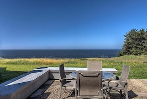 An outdoor seating area with a table and chairs, overlooking a body of water. - Wild Iris | Ocean View Haven with Hot Tub (Sea Ranch)