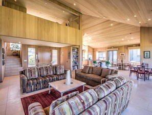 A spacious living area with a high ceiling, built-in bookshelves, and a staircase leading to an upper level.