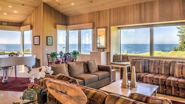 A spacious living area with a piano, sofas, and large windows overlooking the ocean. - Wild Iris | Ocean View Haven with Hot Tub (Sea Ranch)