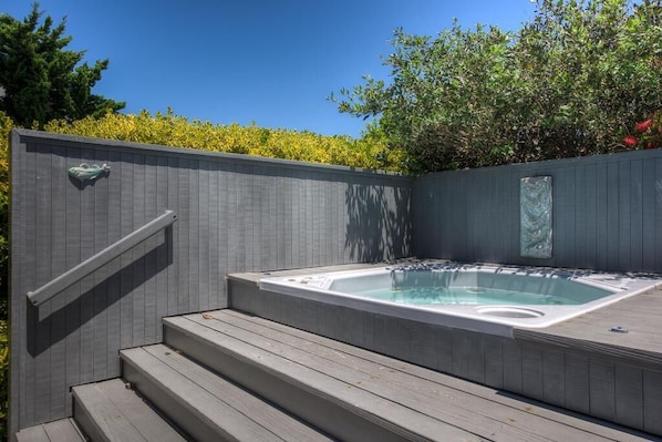 A hot tub with steps leading up to it, surrounded by a wooden deck and a grey wall.