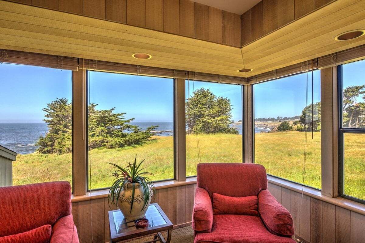 A room with large windows offering a view of the sea and greenery.