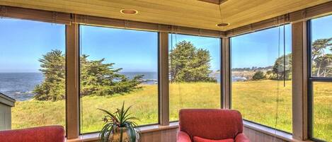 A room with large windows offering a view of the sea and greenery.