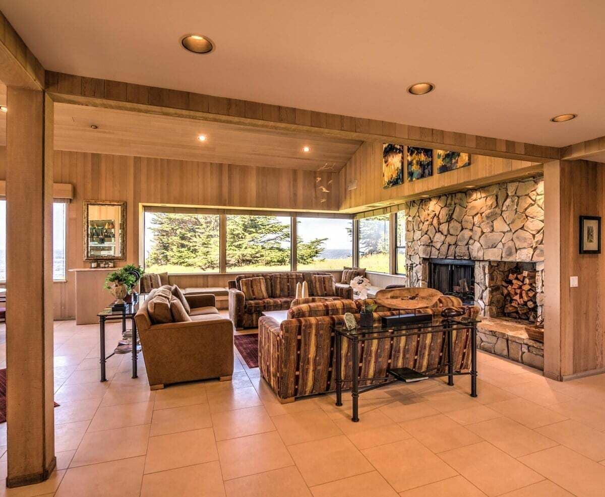 A spacious living room with a stone fireplace, large windows, and a cozy seating area.