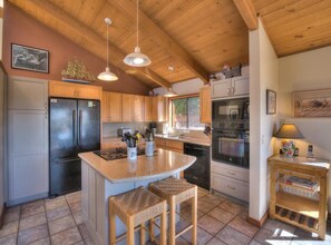 A kitchen with wooden cabinets, a central island with stools, a refrigerator, an oven, and a sink.