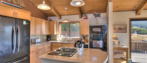 A kitchen with wooden cabinets, a stainless steel refrigerator, a built-in stove, and pendant lighting.