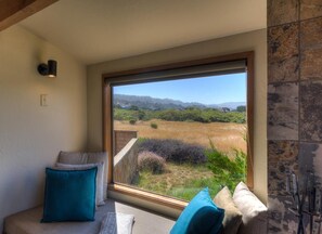 A room with a large window offering a view of a field and distant hills. - Robinsong - Fireplace & Ocean View Relaxation (Sea Ranch)