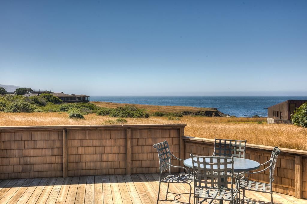 A wooden deck with a table and chairs overlooking a coastal landscape.