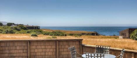 A wooden deck with a table and chairs overlooking a coastal landscape.