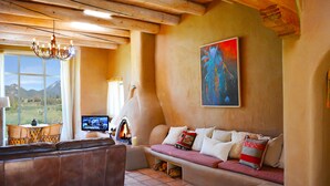 Un salon chaleureux avec une cheminée, un canapé agrémenté de coussins, un téléviseur et une vue sur les montagnes par une grande fenêtre.