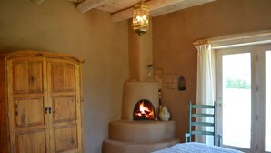 Une chambre avec une armoire en bois, une cheminée, un lit recouvert d’une courtepointe et une vue par la fenêtre.