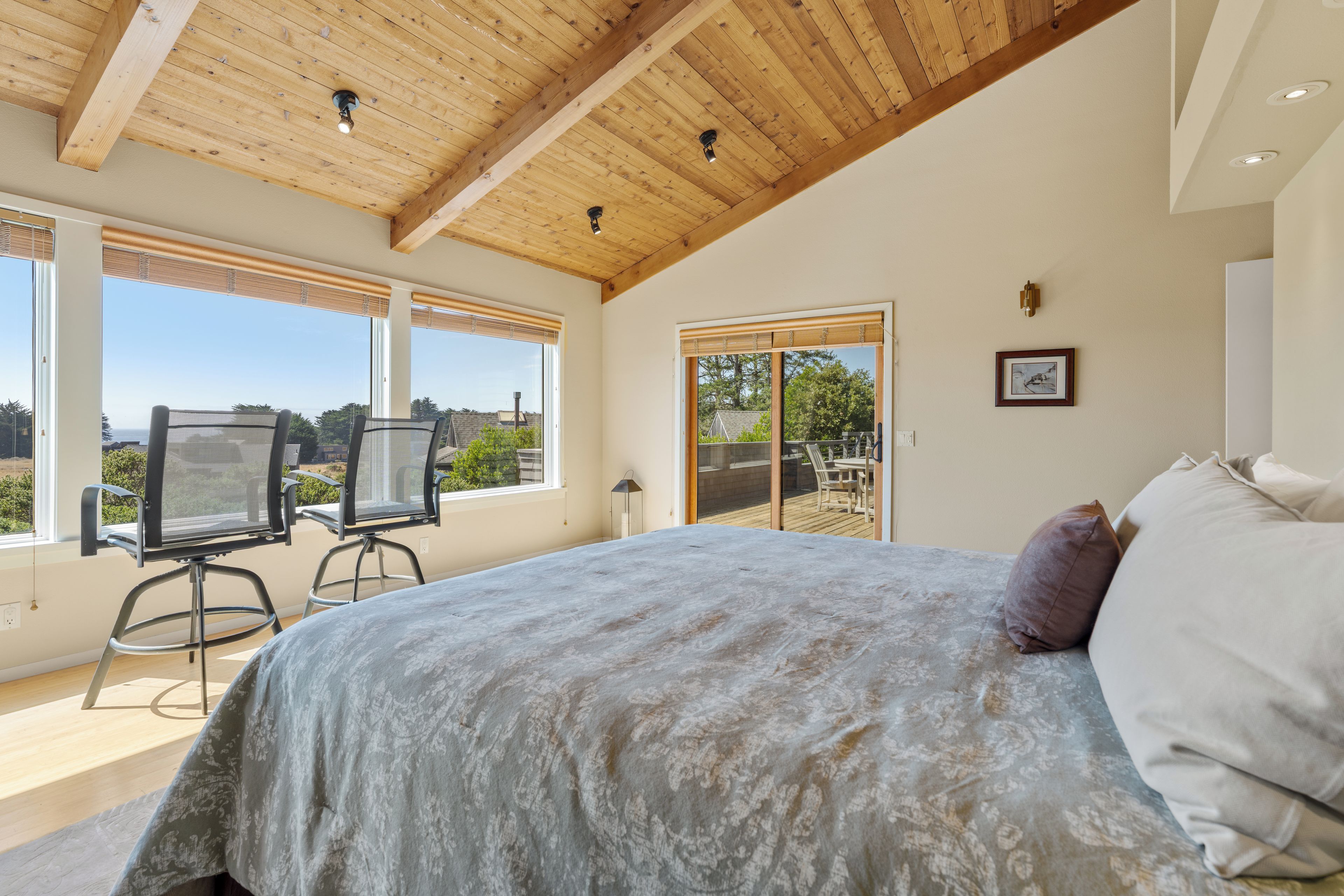 A bedroom with a large bed, a view of the outdoors through a sliding door, and a ceiling with exposed wooden beams.