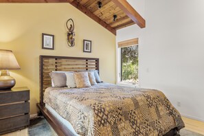 Quarto com cabeceira de madeira, colcha estampada, mesa de cabeceira com abajur e duas fotos emolduradas na parede.
