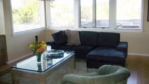Un salon avec un canapé d’angle, une table basse en verre et un fauteuil vert.