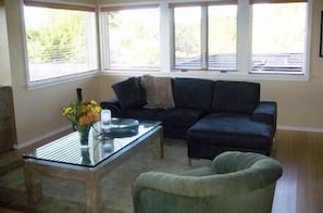 Ein Wohnzimmer mit einem Ecksofa, einem Glastisch und einem grünen Sessel.