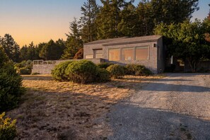 A modern two-story house with a gravel driveway, surrounded by dense trees and shrubs. - Sea Watch - Hot Tub & Ocean Deck Views (Sea Ranch)