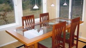 Une table à manger avec des chaises et des luminaires suspendus, dans une pièce dotée de grandes fenêtres.
