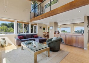 A spacious living area with a glass coffee table, a sofa, and a dining area with wooden cabinets. - Sea Watch - Hot Tub & Ocean Deck Views (Sea Ranch)