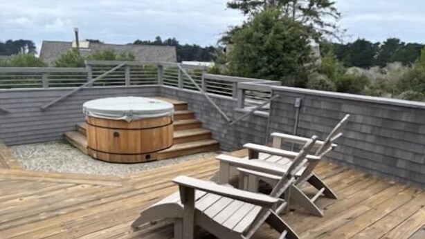 Une terrasse en bois avec un jacuzzi et deux fauteuils Adirondack.
