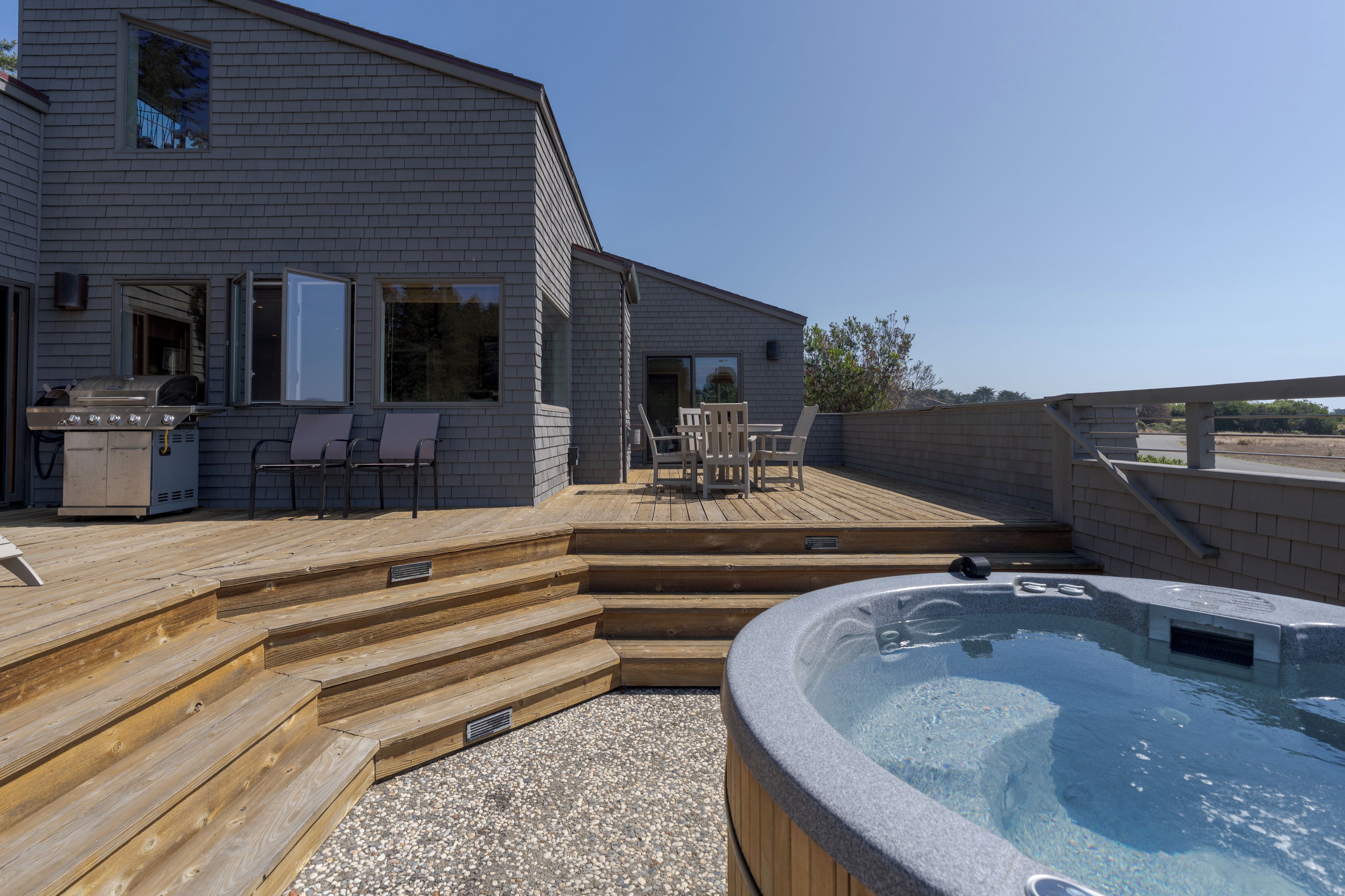 A residential deck with a hot tub, outdoor seating, and a barbecue grill.