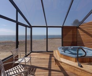 A hot tub with a wooden deck and a view of the ocean.