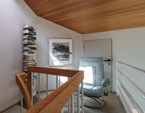 A room with a wooden staircase, a bookshelf, a framed picture, a light blue chair, and a door.