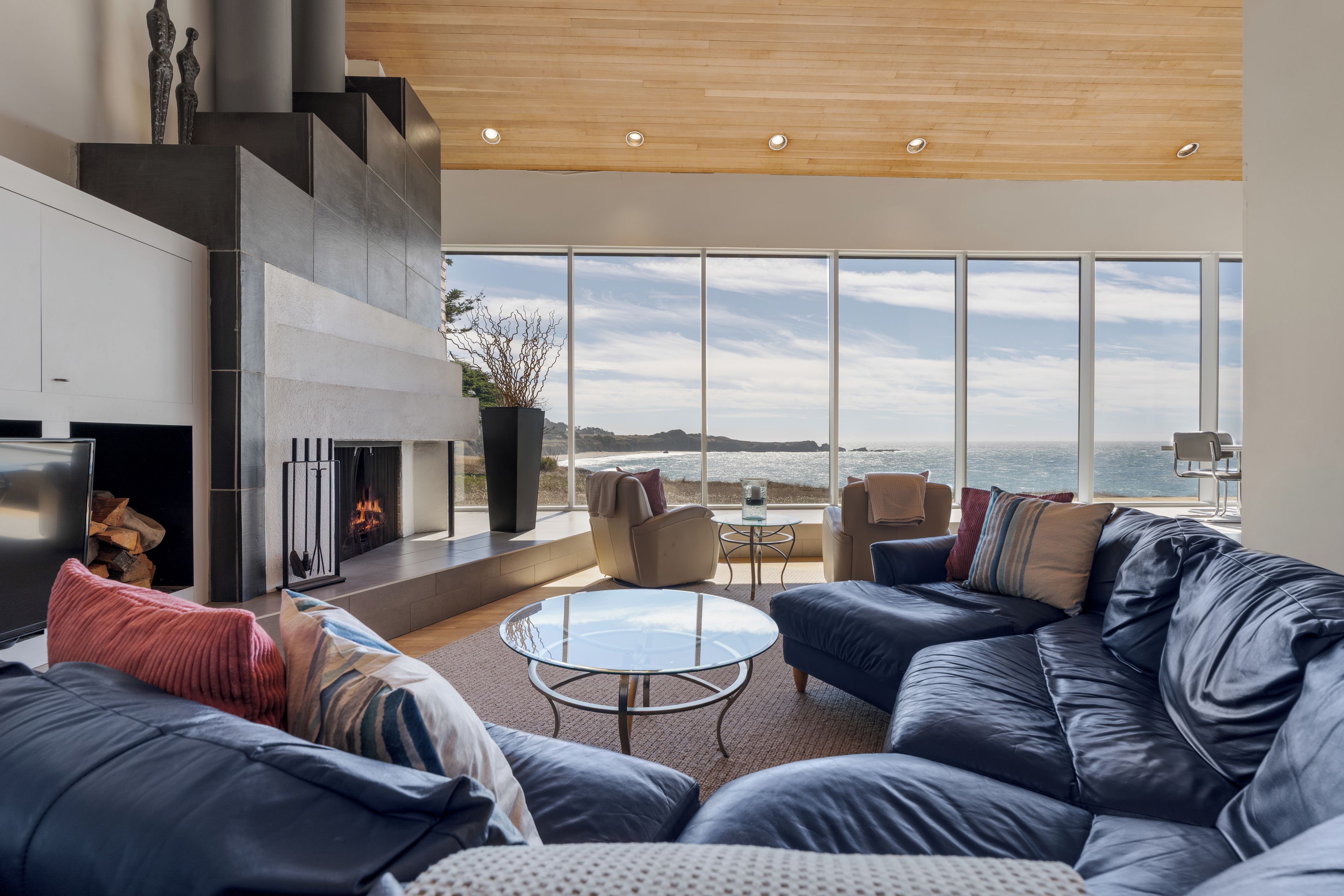 A modern living room with a fireplace, leather sofa, and a large window overlooking the sea.