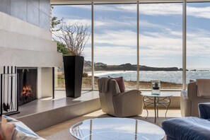 A modern living room with a fireplace, seating area, and a large window overlooking the ocean.