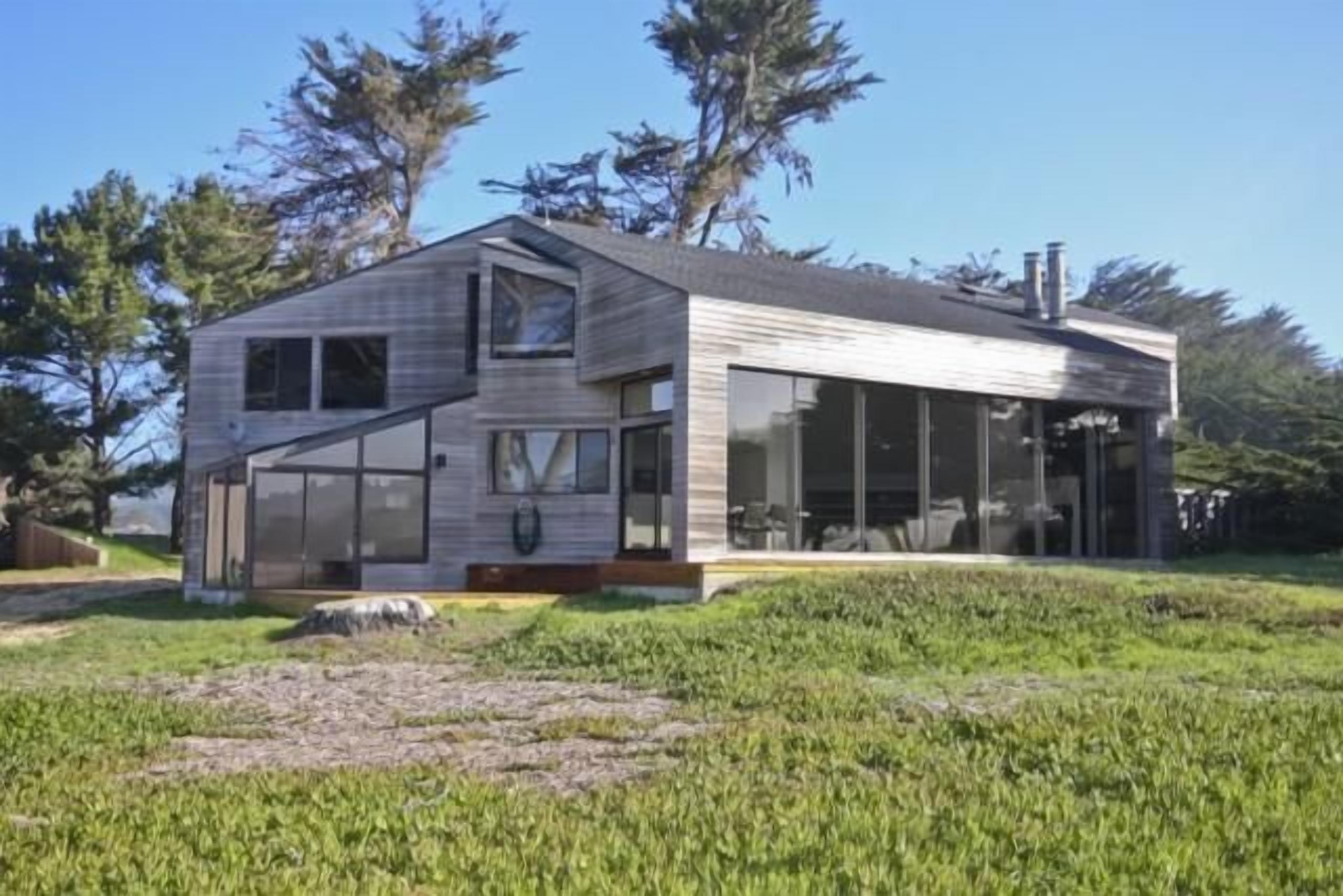 Una casa moderna con techo inclinado, ventanas amplias y un espacio exterior cubierto.