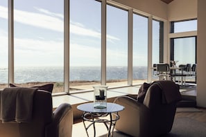 A modern living room with large windows overlooking a coastal view, furnished with leather sofas and a glass coffee table.
