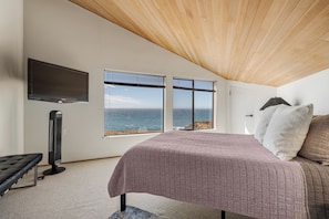 A bedroom with a bed, a TV, a heater, and a view of the sea.