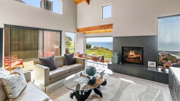 A modern living room with a glass coffee table, leather sofa, and a fireplace. - Sea Walk Retreat | Front-Row Whale Watching Condo (Sea Ranch)