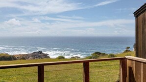 Une vue sur la côte depuis un balcon en bois doté d’une balustrade, donnant sur l’océan et la côte rocheuse.