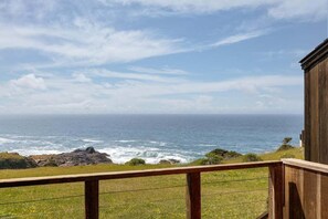 Vista costera desde un balcón de madera con barandilla, con vista al océano y la costa rocosa.