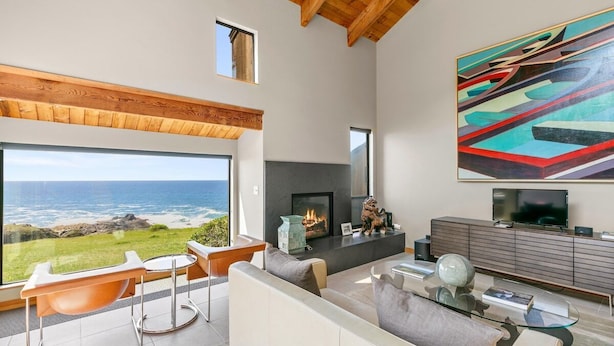 Un salon moderne avec une cheminée, un grand tableau et une vue sur l’océan.