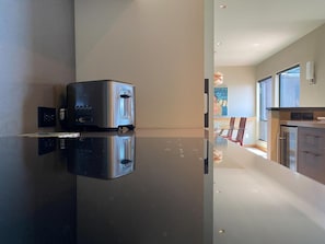 A modern kitchen with a reflective countertop, a built-in oven, and a dining area with a table and chairs.