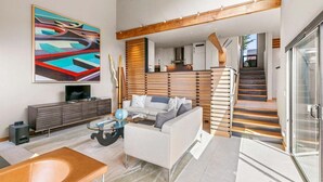 Un salon moderne avec un canapé, une table basse et un téléviseur. Un escalier mène à un niveau supérieur.