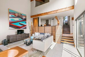 Una sala de estar moderna con un sofá, una mesa de centro y un televisor. Se ve una escalera que sube a un nivel superior.