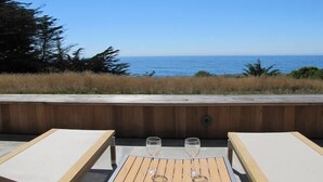 An outdoor seating area with two tables and chairs, overlooking a coastal view.