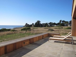 A patio with two lounge chairs overlooking a grassy area and a body of water.