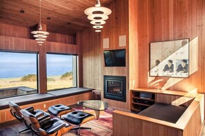 Een modern interieur met een open haard, zithoek en grote ramen met uitzicht op een strand.