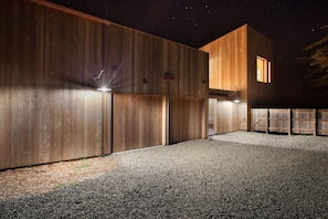 A modern building with a wooden exterior and a gravel driveway at night.