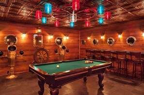 Een biljart met biljartballen, houten wanden en een plafond met zichtbare balken en hangende lampen.