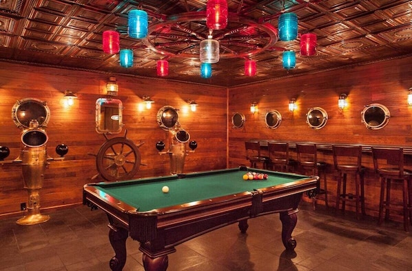 A pool table with billiard balls, wooden walls, and a ceiling with exposed beams and hanging lights.