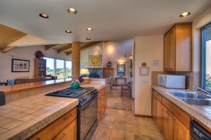 A spacious kitchen with a large island, wooden cabinets, and a stone backsplash. - Sea Gate - Private Meadow & Ocean Views (Sea Ranch)