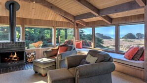 A cozy living room with a fireplace, large windows, and comfortable seating.