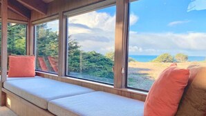 A room with a built-in bench seating area with cushions, large windows offering a view of the outdoors.